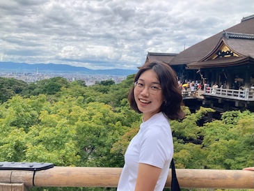 A person smiling outdoors with a view behind them.
