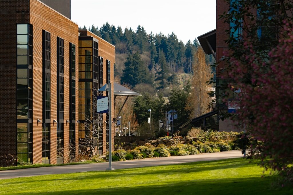 Modern brick campus buildings with lawn, trees and a forested hillside.