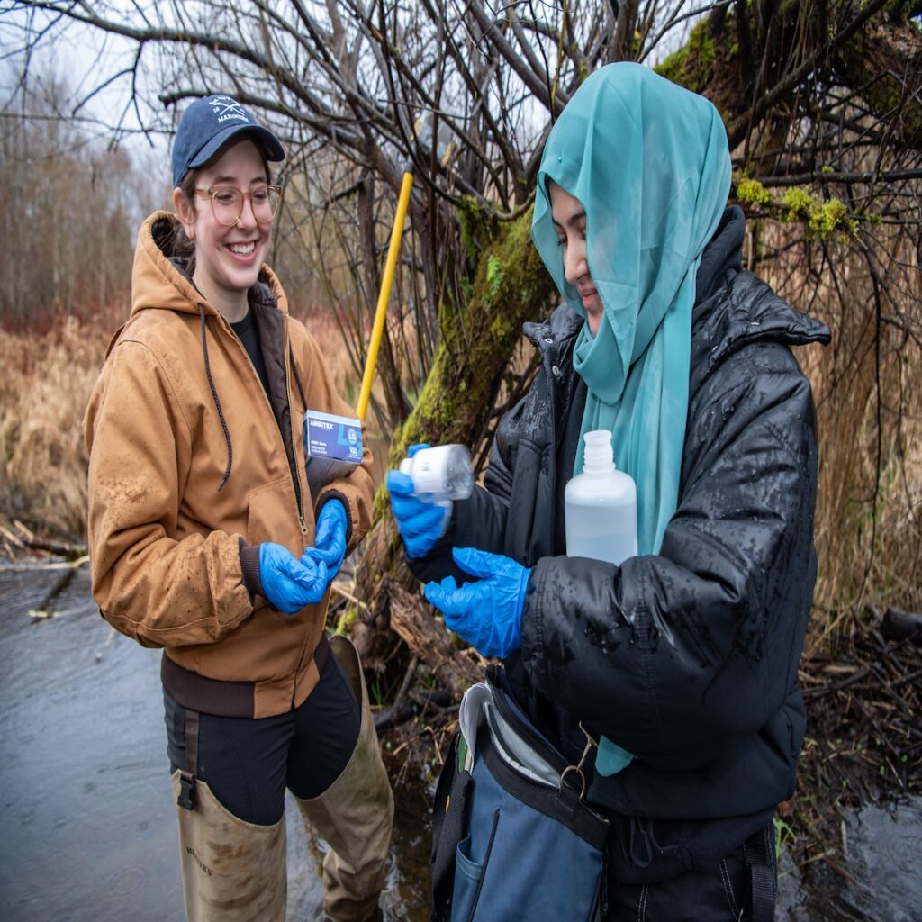 People collecting water from a wooded stream.