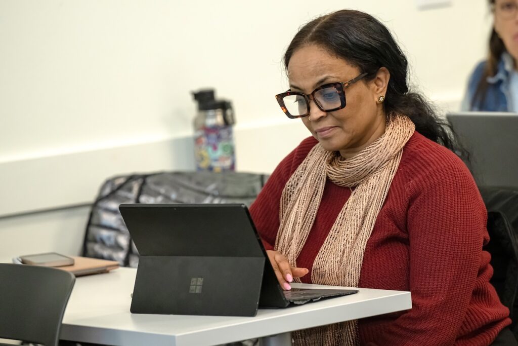 Woman using a tablet at a table in a classroom or meeting space.