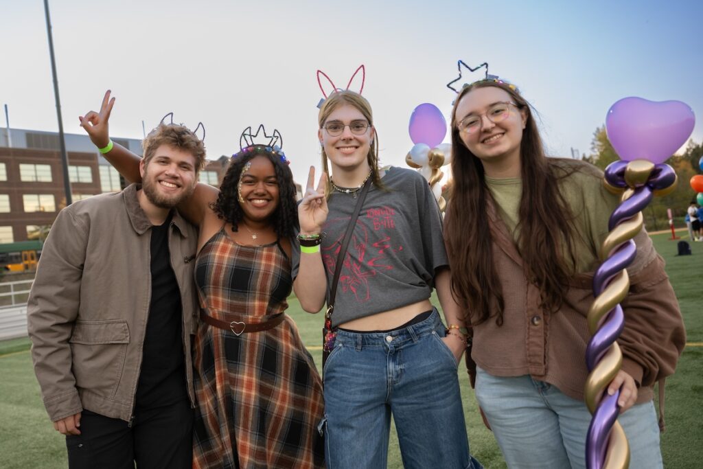 Four smiling students at an outdoor campus event.