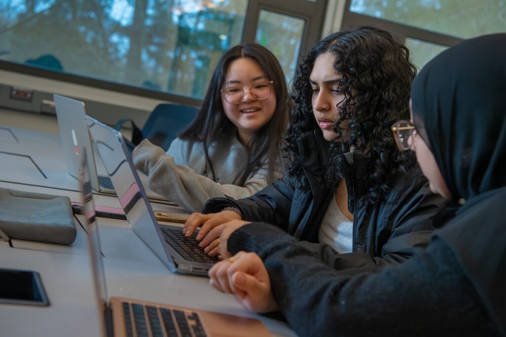 Three students collaborate on laptops.
