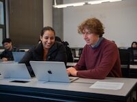 Two people collaborating at a table with laptops