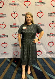 Melanie is posing in front of a backdrop that says, HEB Excellence in Education Awards.  