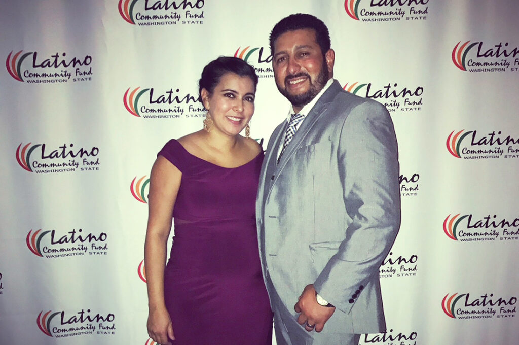 Hector Valencia and his wife, Mariela, dressed up for an event, posing in front of a background that says "Latino Community Fund Washington State." 