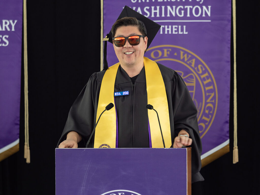 Jason Moon in graduation regalia, speaking at a podium