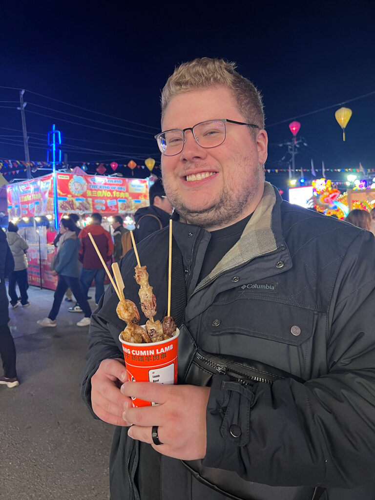 Taylor at a night market with a cup of meat skewers.