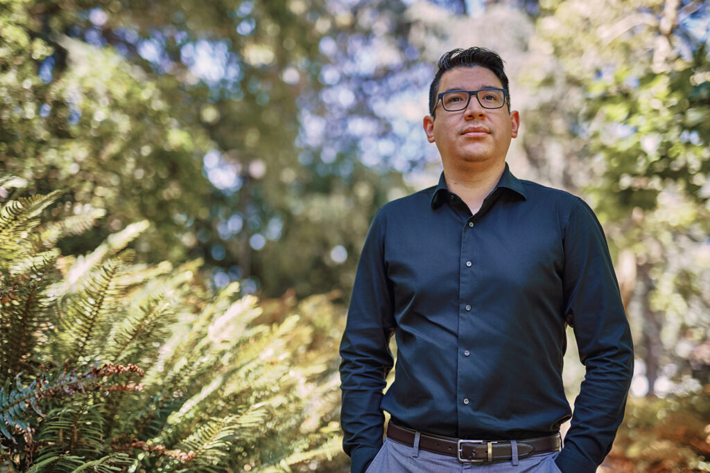 Alfred, wearing a black shirt, in front of ferns and other greenery.