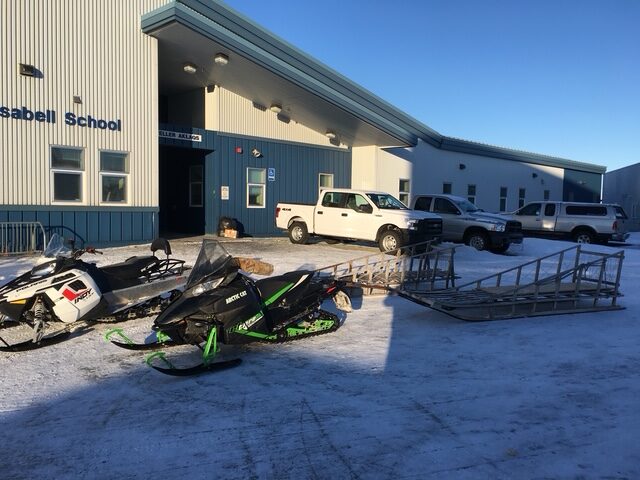 Snowmobiles and trucks outside of a school building