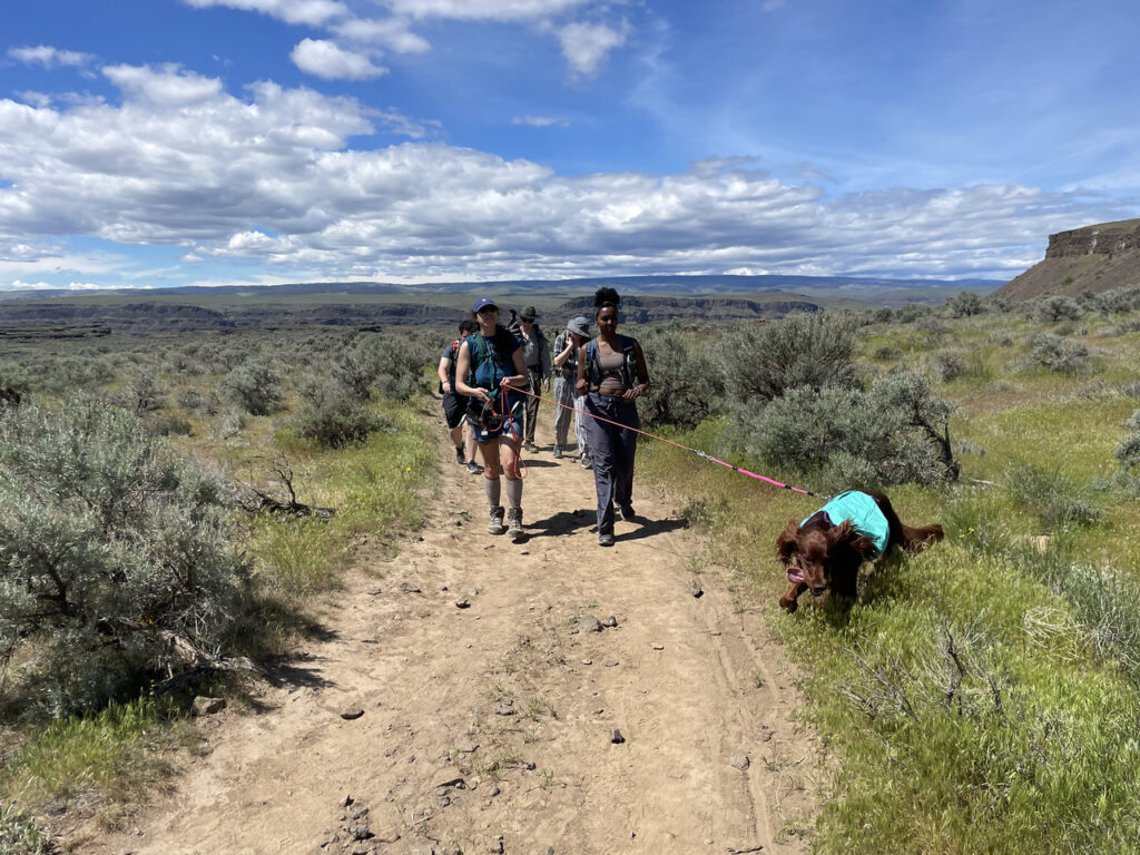 Students hiking on a dirt trail with a service dog