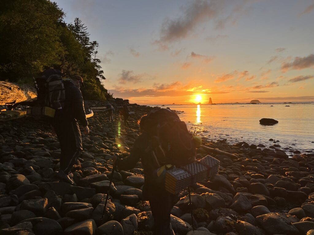Students hiking on rocks along the beach at sunset