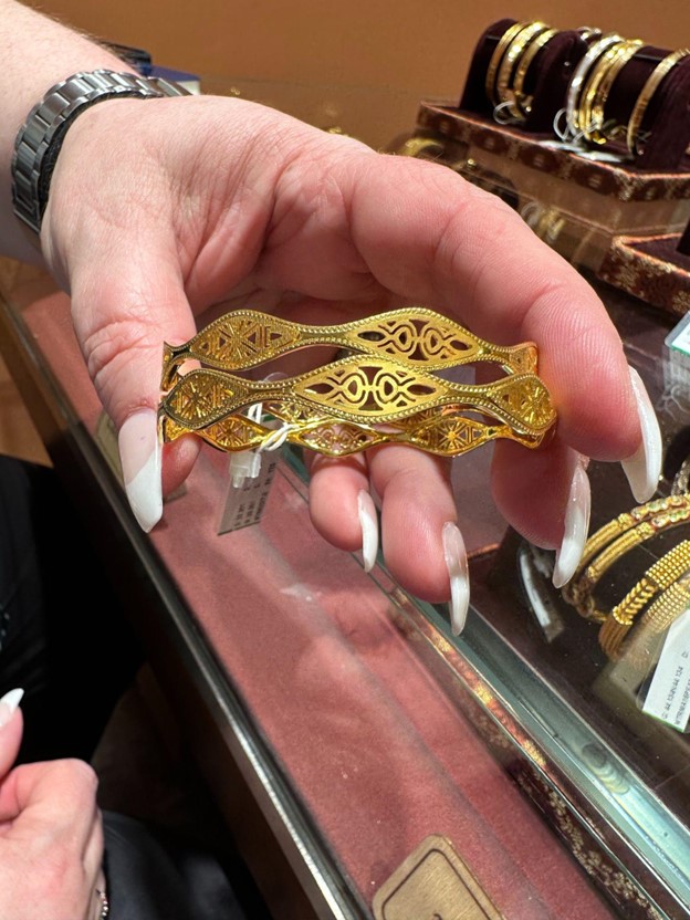 A person holding two ornate gold bangles