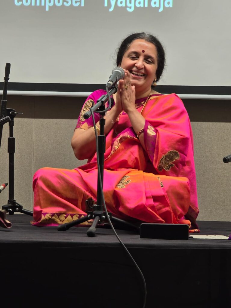 A classical Indian music singer sitting on a stage and performing in front of a microphone