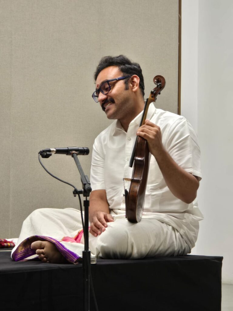 A classic Indian music performer sitting on stage and holding a violin