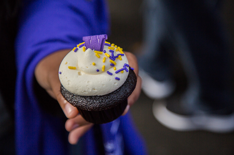 A person holding out a cupcake with a purple W on it