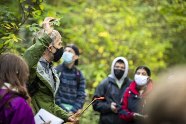Dave Stokes, professor, holds leaves in his hand while teaching class in a forest