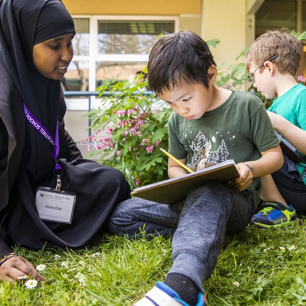 NextGen student tutors two children in the grass at their school.