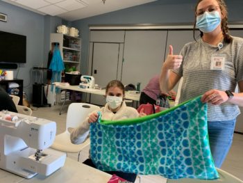 Fallon Zollar holds up a quilt with student at the ABC