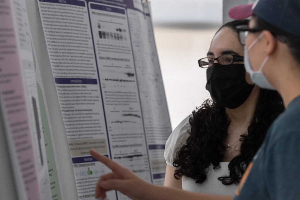 two students look and point at a research poster