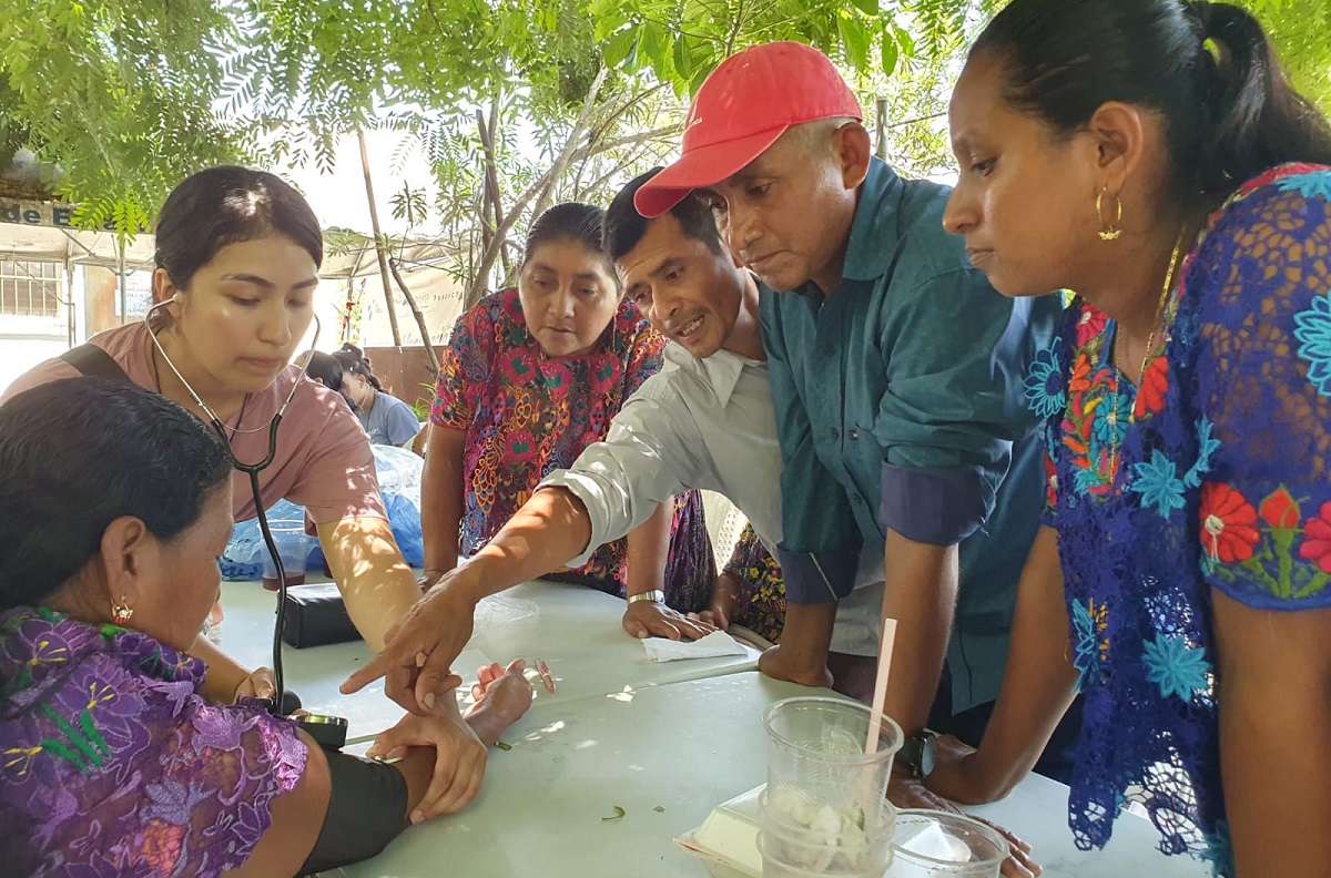 Student shows Guatemalan adults how to use a blood pressure cuff while outdoors at a picnic table