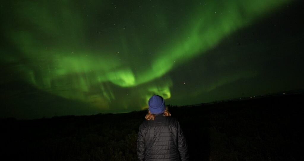 Woman is looking at a brightly colored green sky, the aurora borealis.