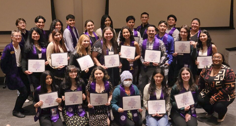 Students pose with certificates during LLI graduation, wearing purple stoles.