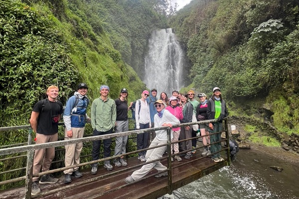 student and faculty group on bridge in front of waterfall and tropical jungle