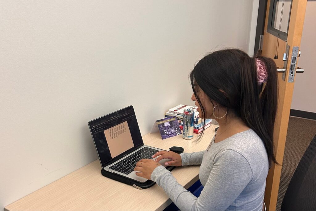 A student sits at a small desk typing on a laptop