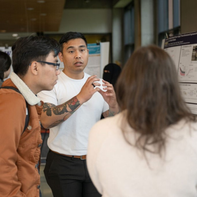 Students talk with a listener and present their research posters