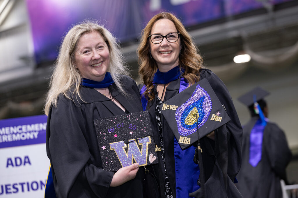 Mary and a friend, both in graduation regalia, show off their decorated caps.