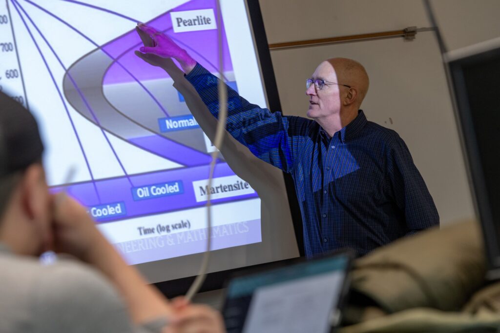 Bill Anderson teaches a class, pointing at a presentation of a graph