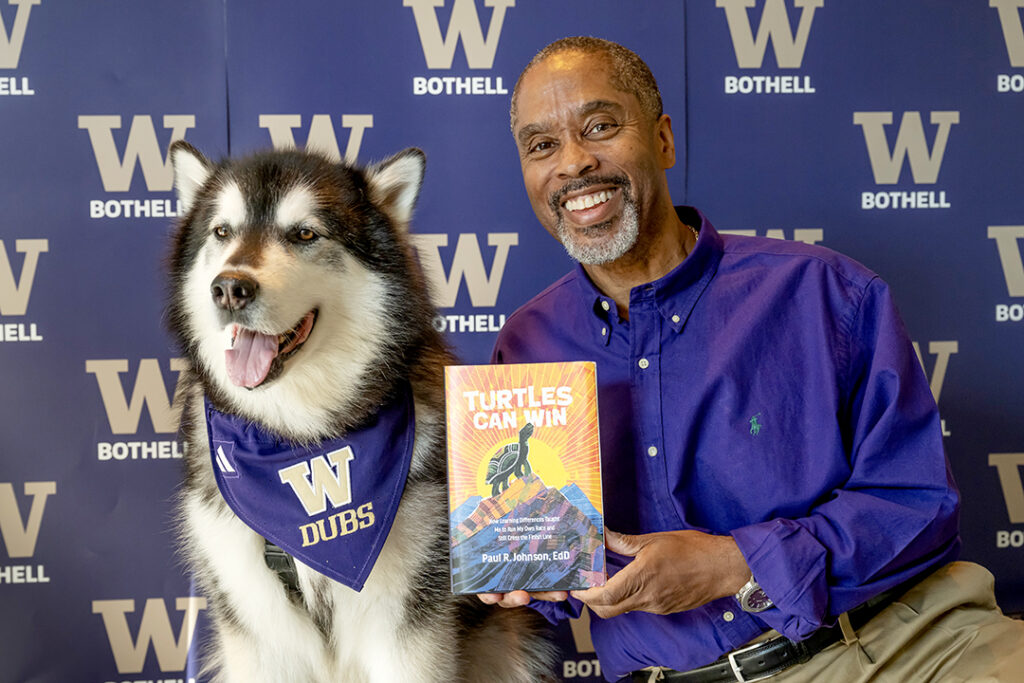 Paul Johnson smiles beside Dubs while holding his memoir, “Turtles Can Win,” at a UW Bothell recognition reception.
