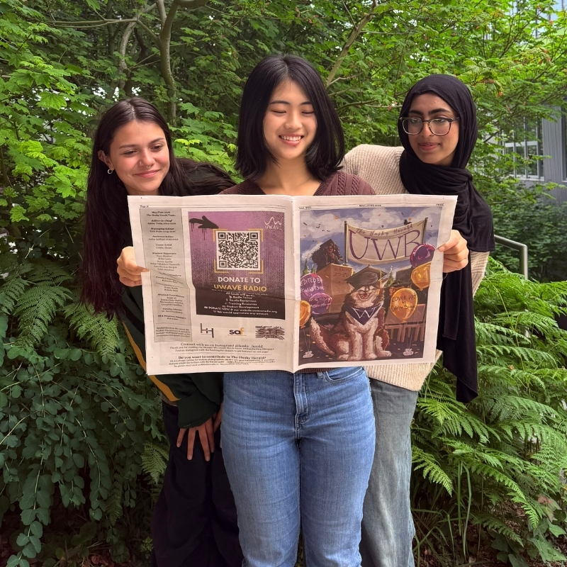 Ashley Tsang, center, holds an issue of the Husky Herald while posing outdoors with two members of the newspaper’s editorial team.