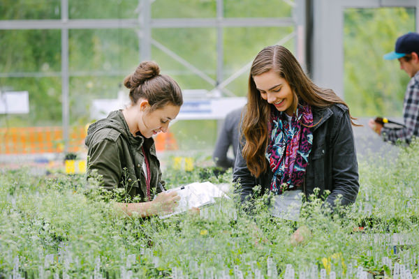 two students writing down notes in a blooming greenhouse