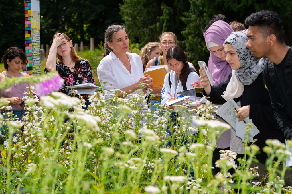 professor teaching to a group of students outside in front of white flowers