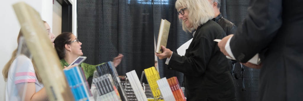 A person showing off a book to two people at a book selling table