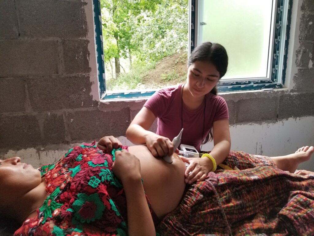 A person holds a fetal heartbeat monitor over a woman's stomach.