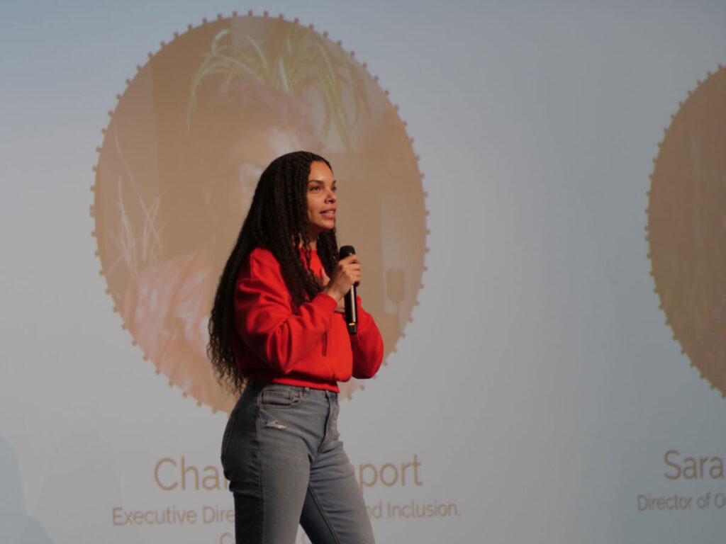 A person with a microphone in front of a large screen.