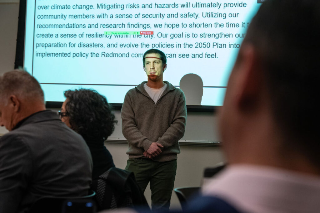 A person presenting in front of a projector screen.