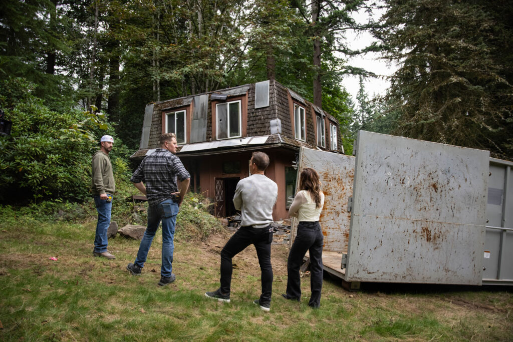 Four people stand outside looking at a house.