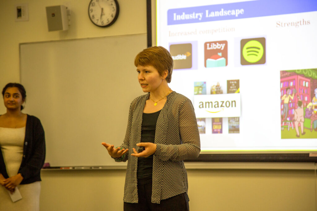 A person presenting in front of a projector screen.