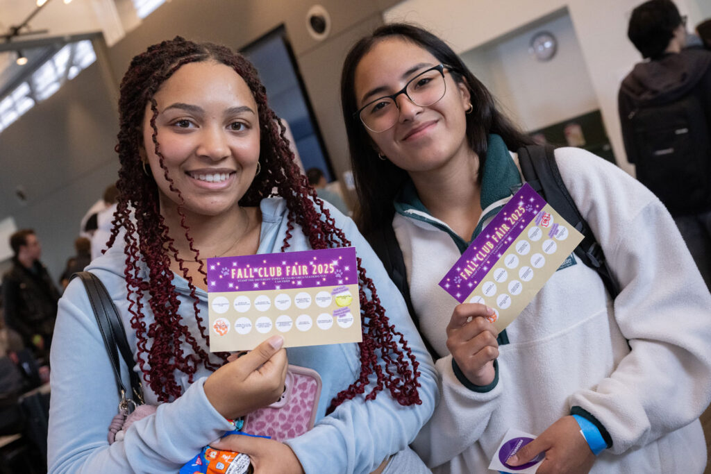 Two people hold up punch cards for the "Fall Club Fair 2025."