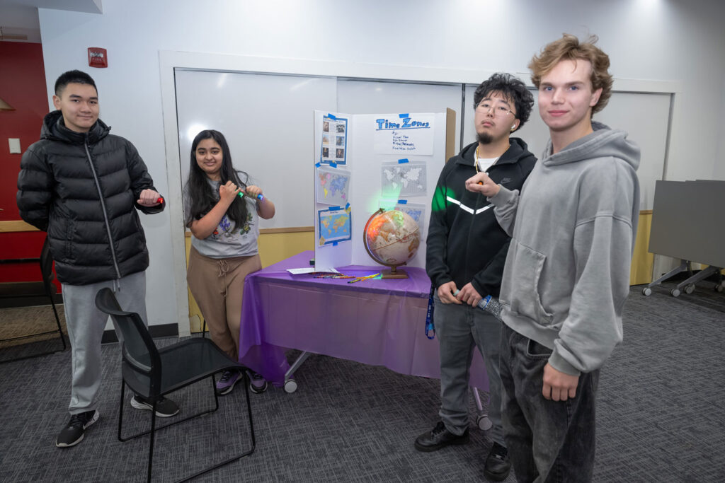 Four people next to a poster on time zones.