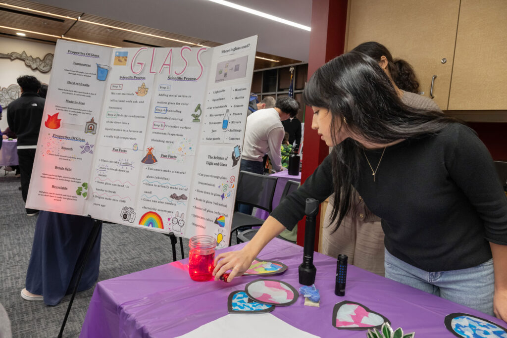 A person shining a light through a glass of colored liquid.