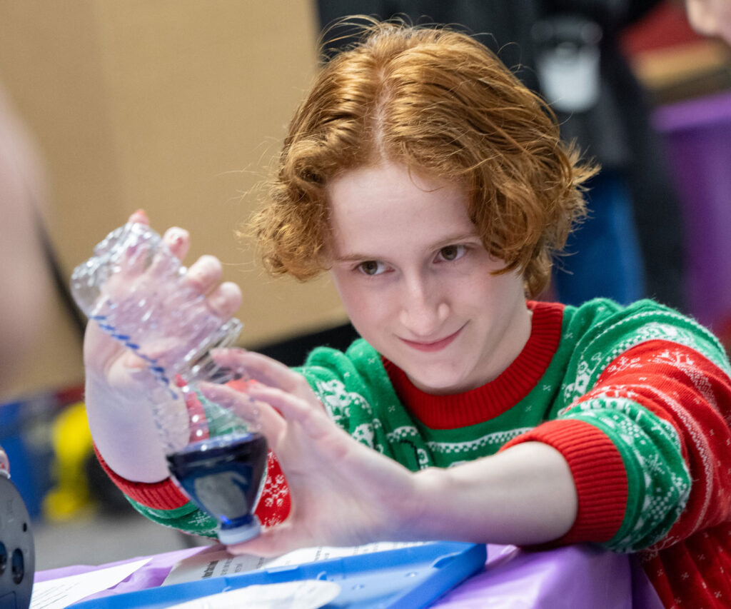 A person pouring a liquid between two halves of a water bottle.