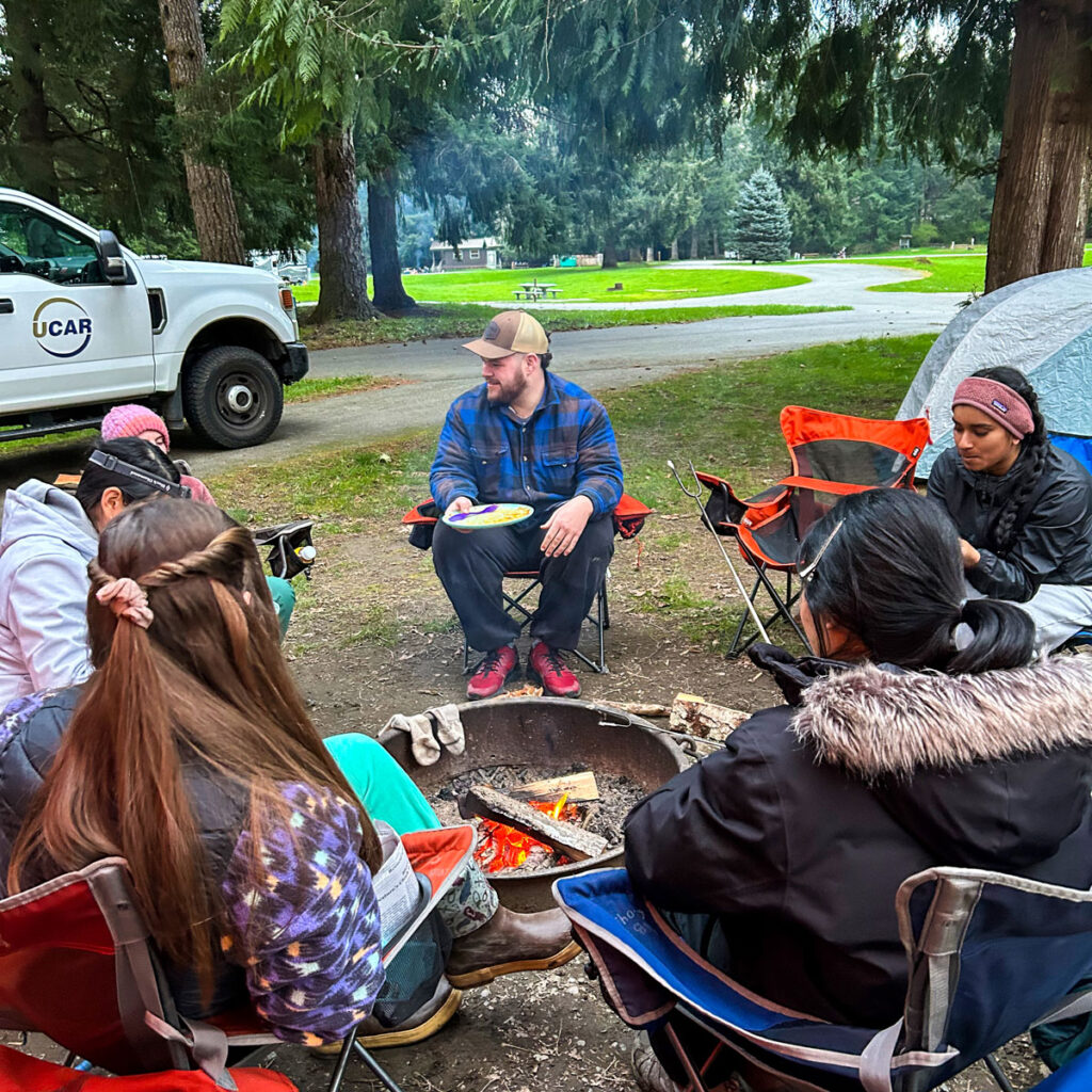 A group of people sit around a campfire.