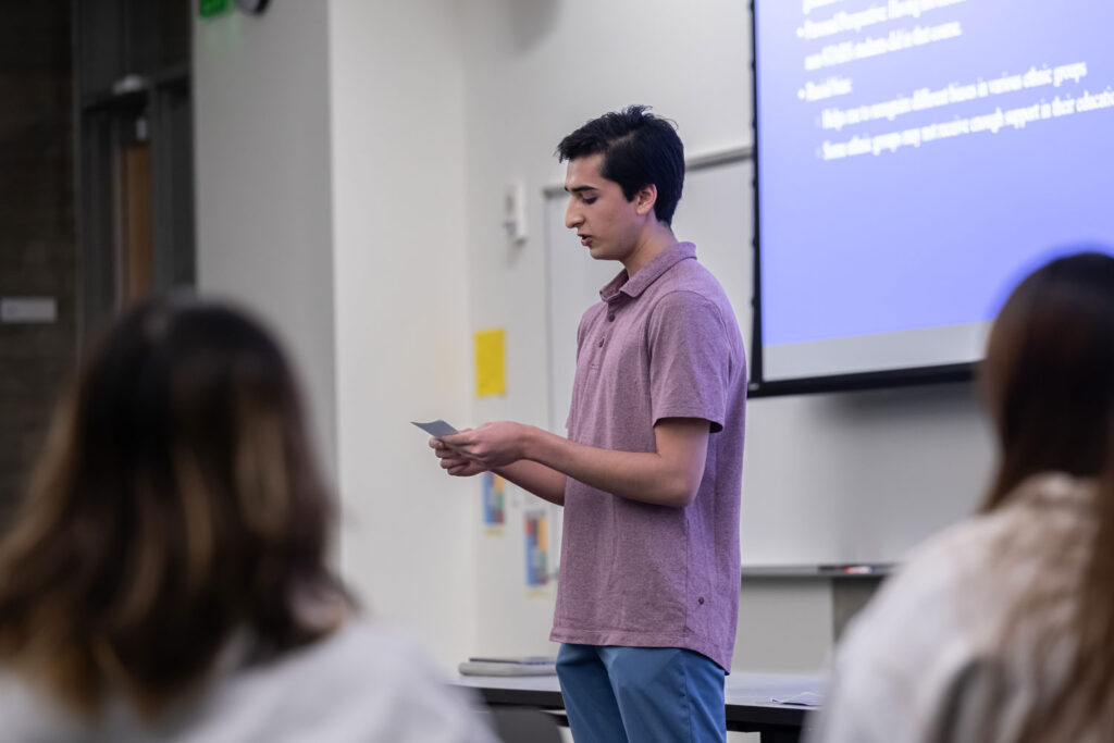 A person presenting in front of a projector screen.