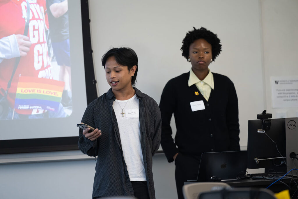 Two people presenting in front of a projector screen.