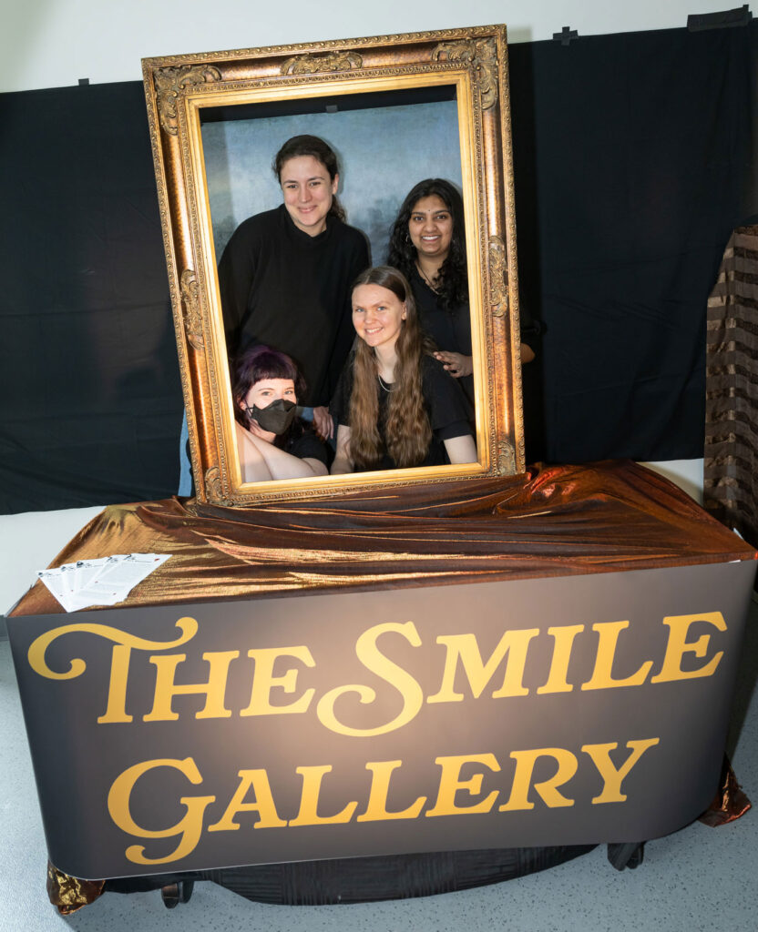 Four people pose behind a picture frame.