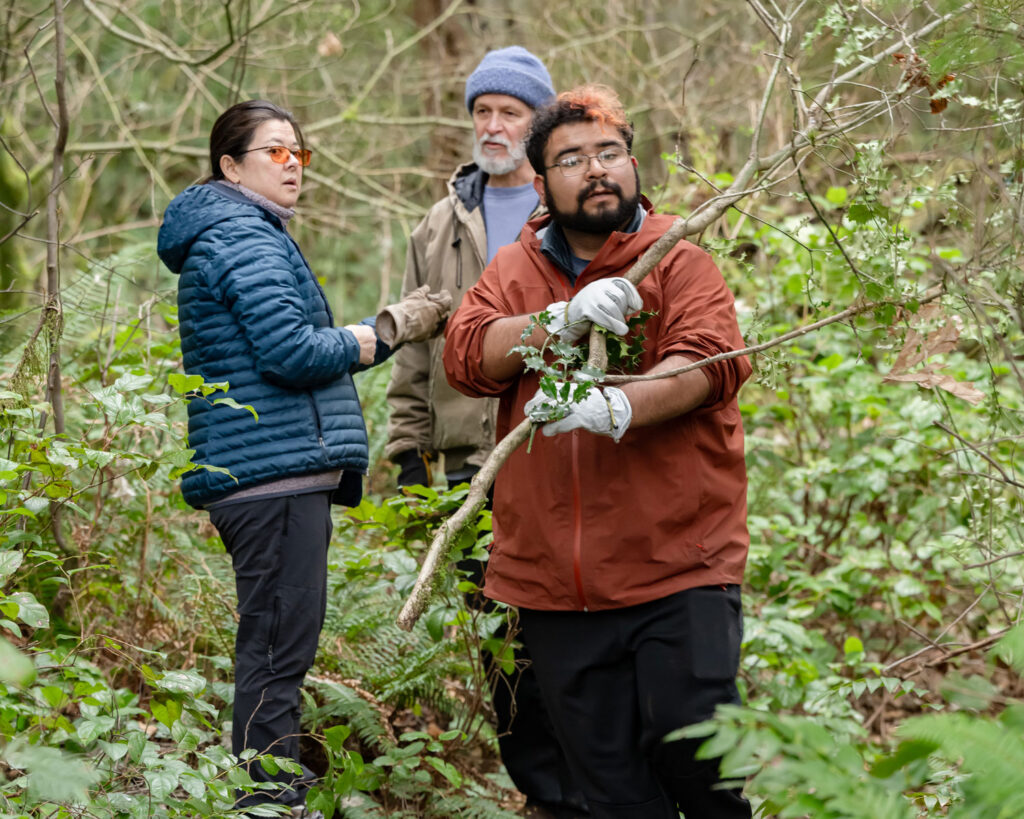 A person holding a branch with two people in the background.